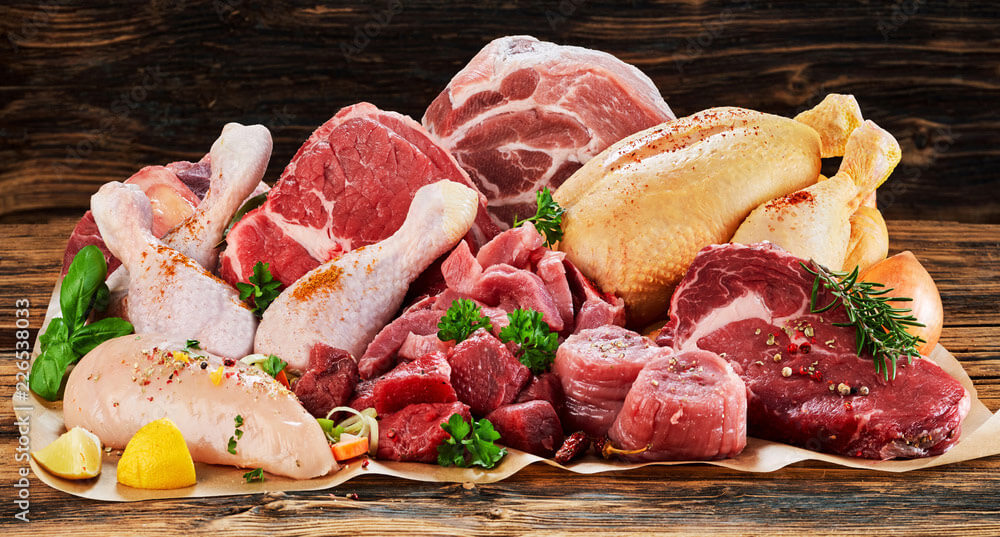 A grouping of various types of meats, like poultry, steak, and pork on a piece of parchment paper on a wooden table