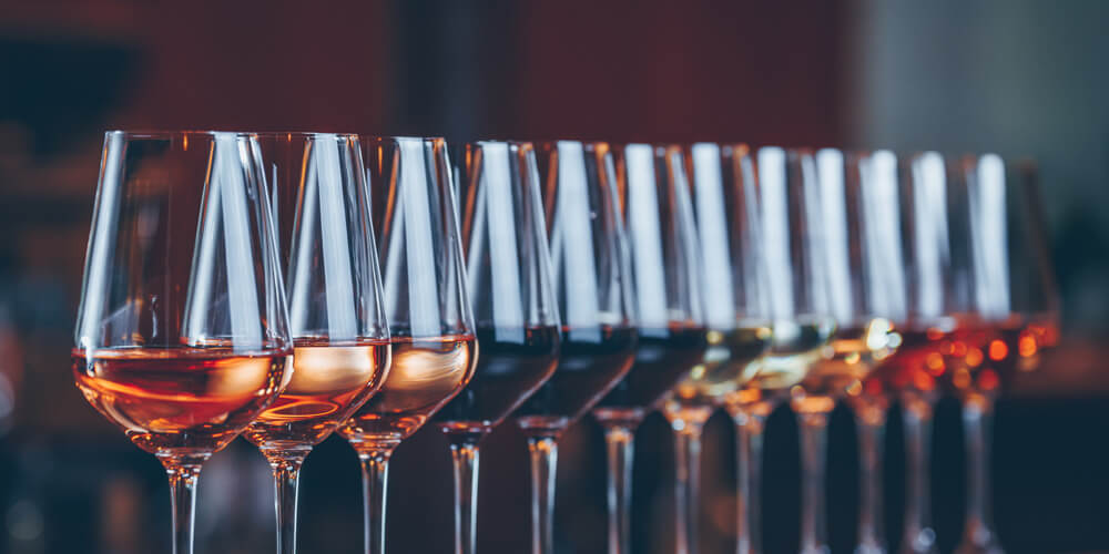 A symmetrical row of 12 wine glasses filled with the same amount of wine of different wine varietals