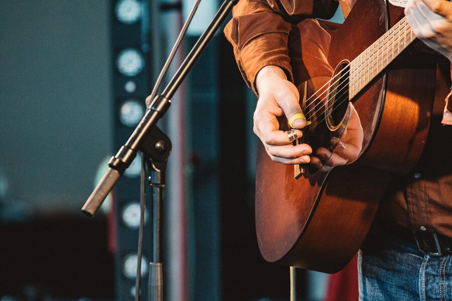 Close up of a person playing a guitar in front of a microphone stand while playing live music