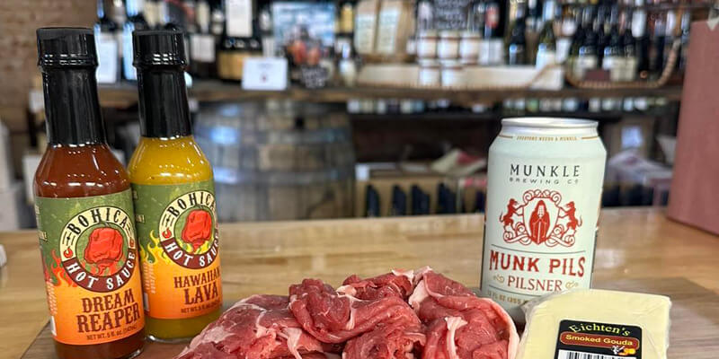 Beer, hot sauce, cheese, and cuts of meat displayed on a cutting board