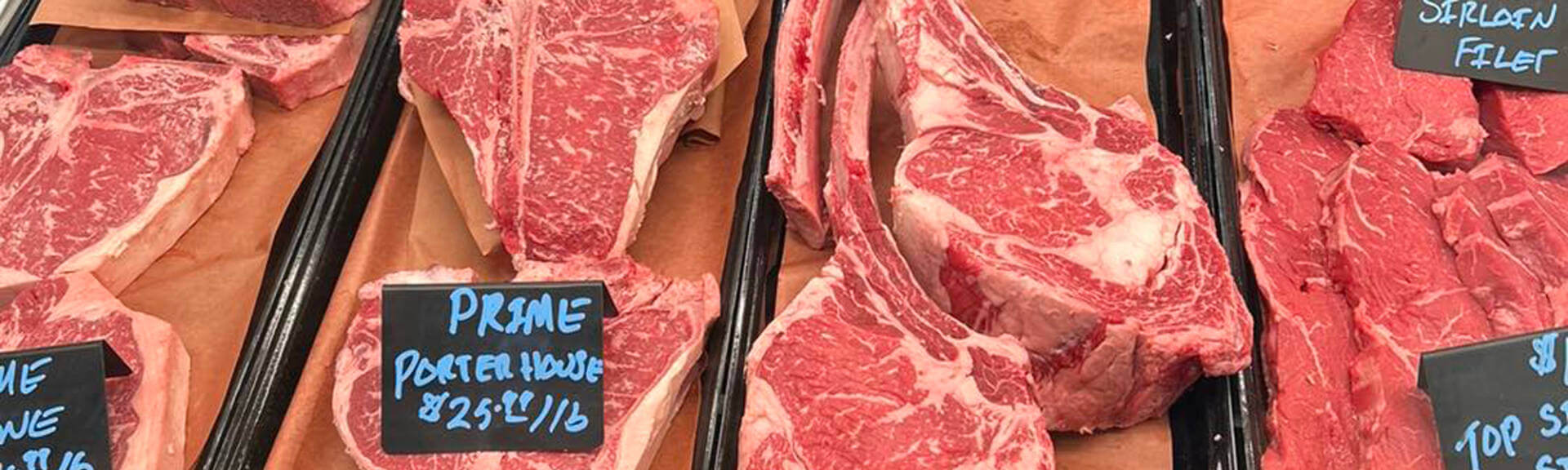 Close up photo of various cuts of meat including Prime Porterhouse in the butcher area