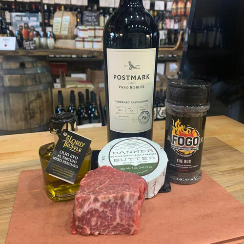 A display of a bottle of wine, olive oil, cheese, and spices next to a marbled cut of meat