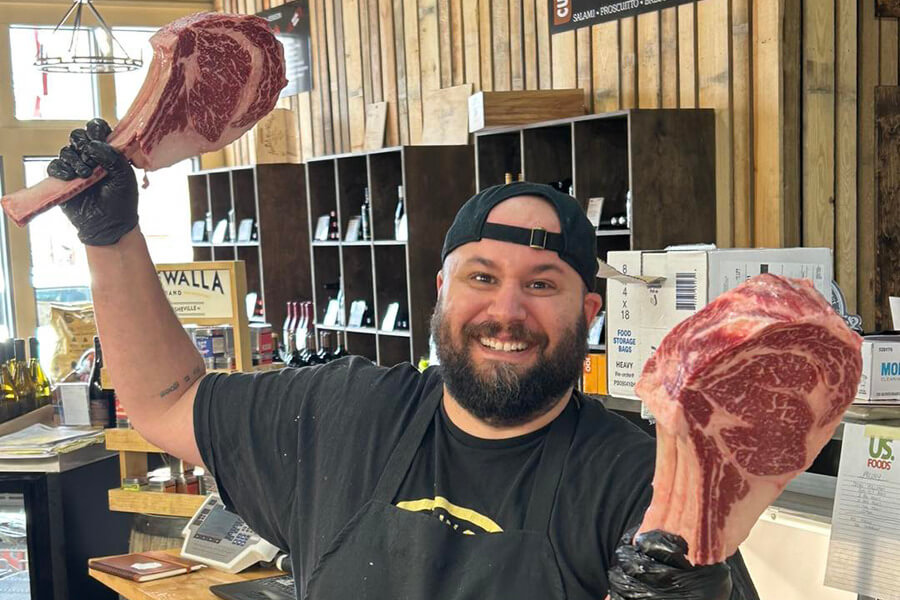 The butcher at Stock & Barrel holding up two very large tomahawk steak cuts